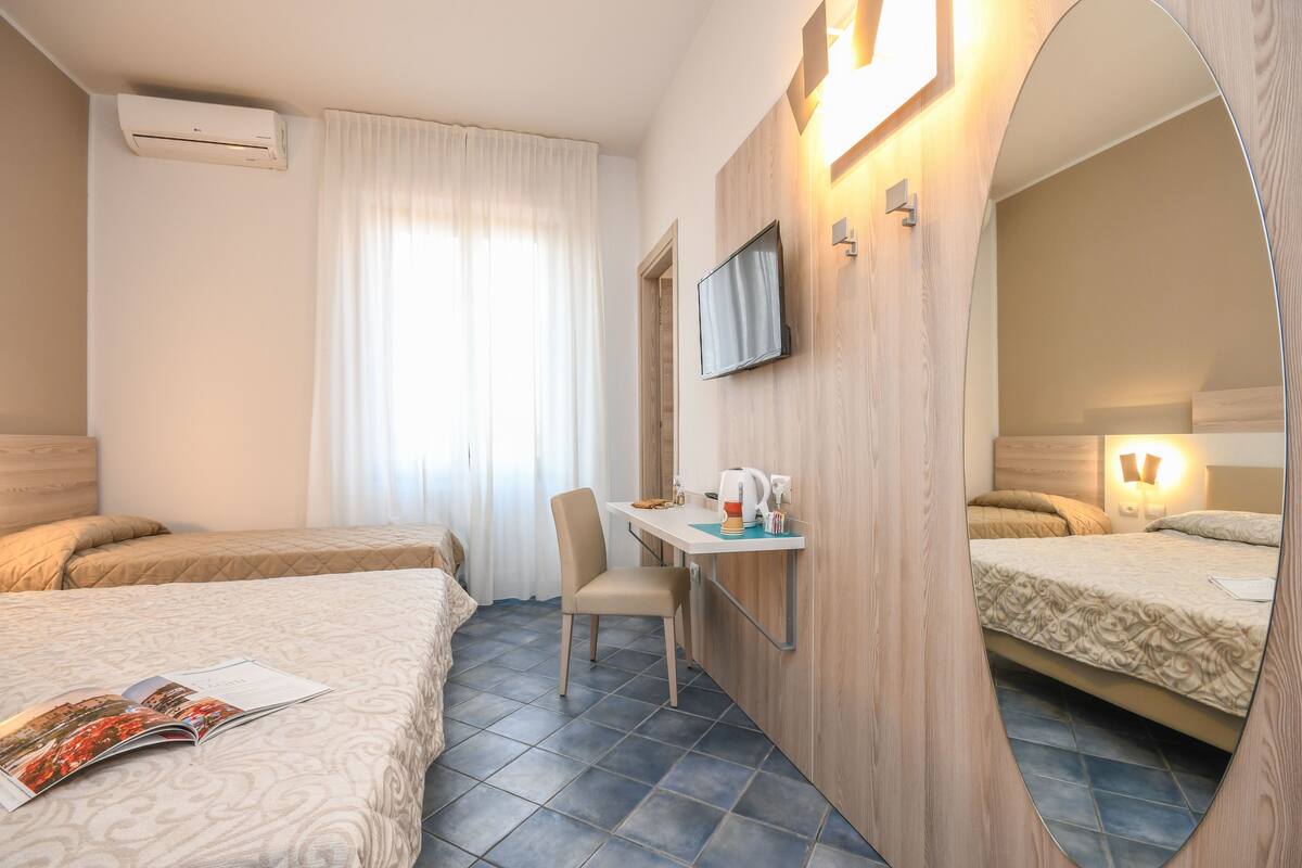 Habitación de hotel con dos camas, un escritorio con una silla, un televisor de pantalla plana y un espejo.