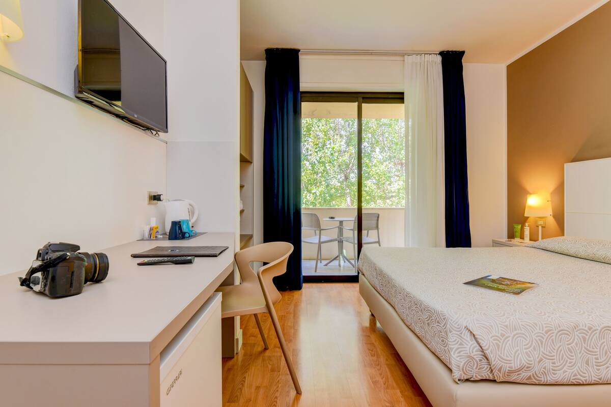 Habitación de hotel con escritorio, silla, cama y vistas al exterior.