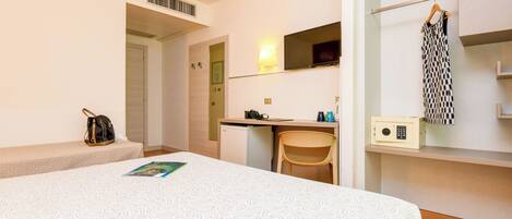 Una habitación de hotel con cama, escritorio, silla, armario, espejo y una pequeña kitchenette.