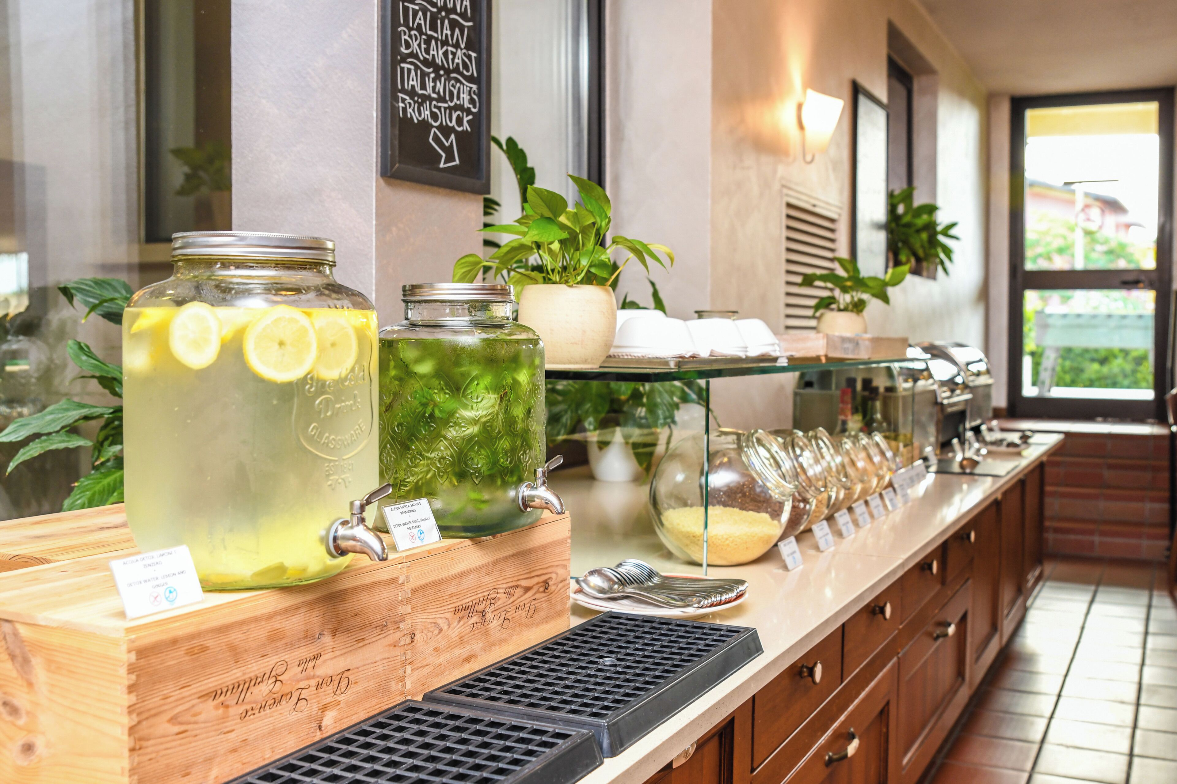 Ein Frühstücksbuffet mit verschiedenen Speisen und Getränken, darunter eine Limonadenflasche und ein Eisteekrug, mit einem Schild, das italienische Frühstücksangebote anzeigt.
