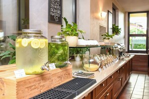 Una barra de desayuno con diversas opciones de comida y bebidas, incluyendo un tarro de limonada y una jarra de té helado, con un cartel que indica opciones de desayuno italiano.