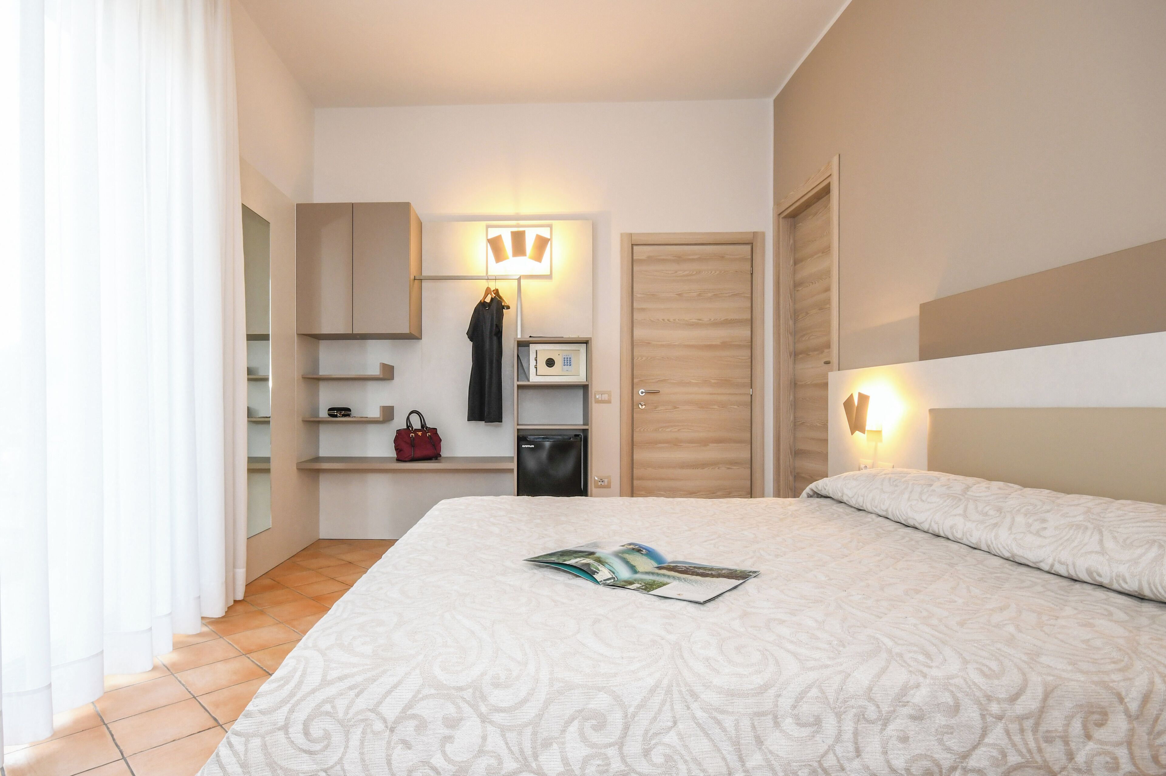 Ein Hotelzimmer mit einem Bett, einem Kleiderschrank, einem Schreibtisch mit Lampe und einem Koffer auf dem Boden.