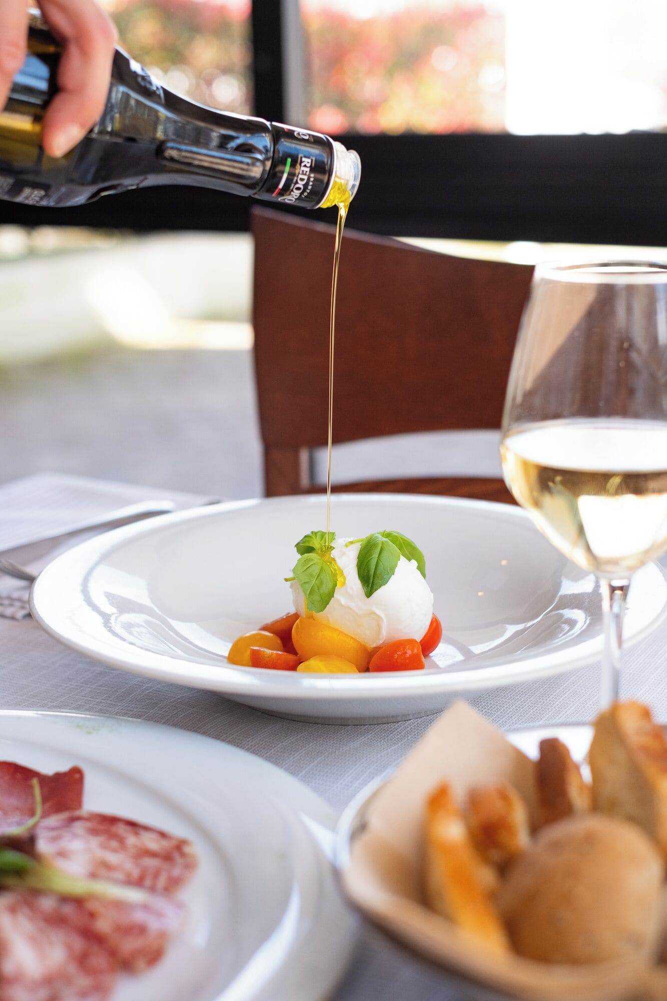 A dessert with a bottle of sauce being poured, a glass of white wine, and plates with food.