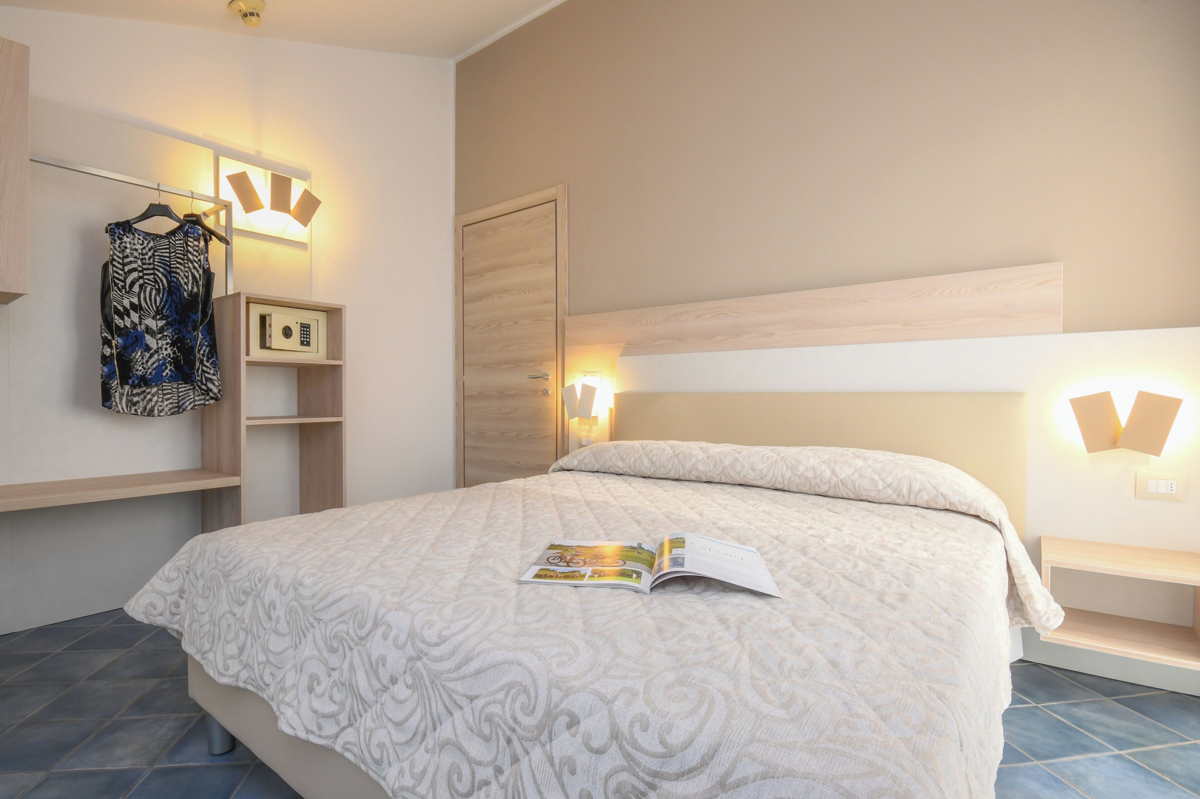 A neatly arranged bedroom with a bed, a bedside table, a nightstand, a wardrobe, and a hanging garment rack.