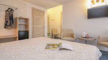 Una habitación de hotel con cama, escritorio pequeño, silla, televisor y armario.