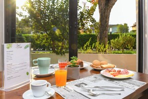 Une table de petit-déjeuner avec un menu, une tasse de café, un verre de jus d’orange, une assiette de nourriture et un journal.