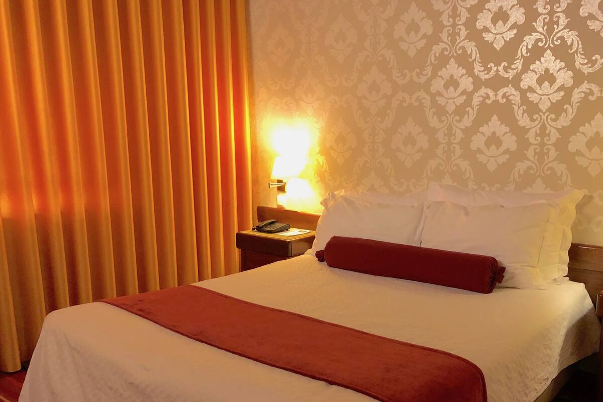 A hotel room with a bed, a nightstand, a lamp, and a curtain.