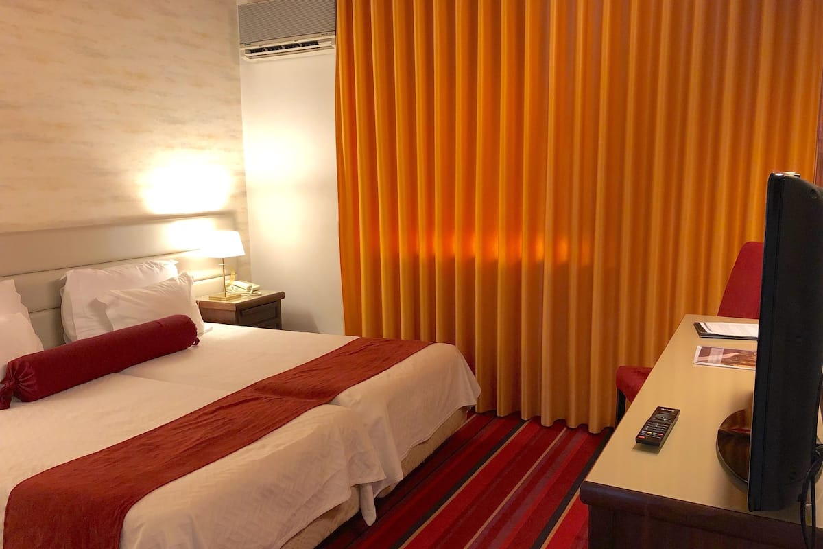 A hotel room with a bed, a desk, a lamp, a remote control, and curtains.