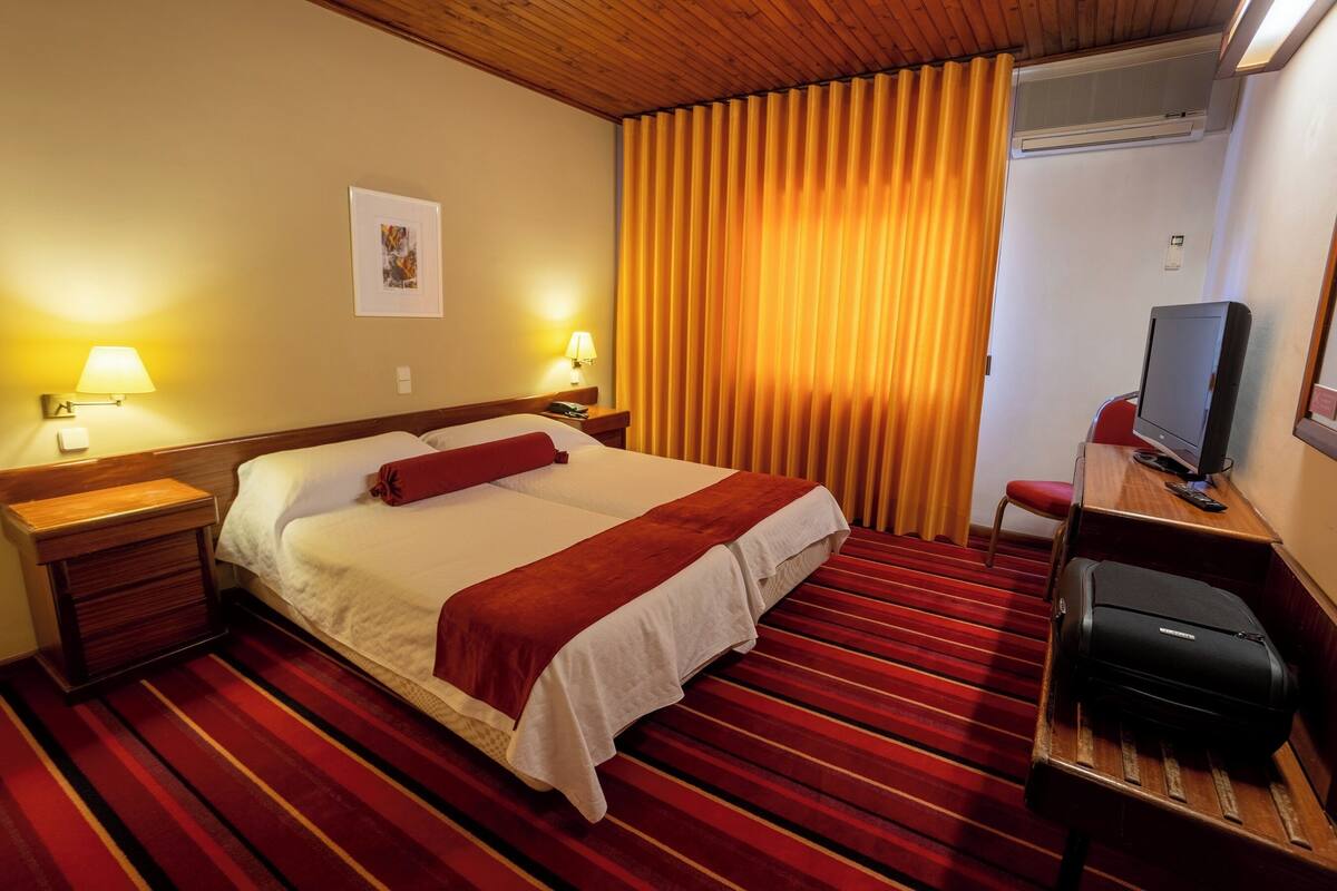A hotel room with a large bed, two bedside lamps, a television, and a desk with a chair.