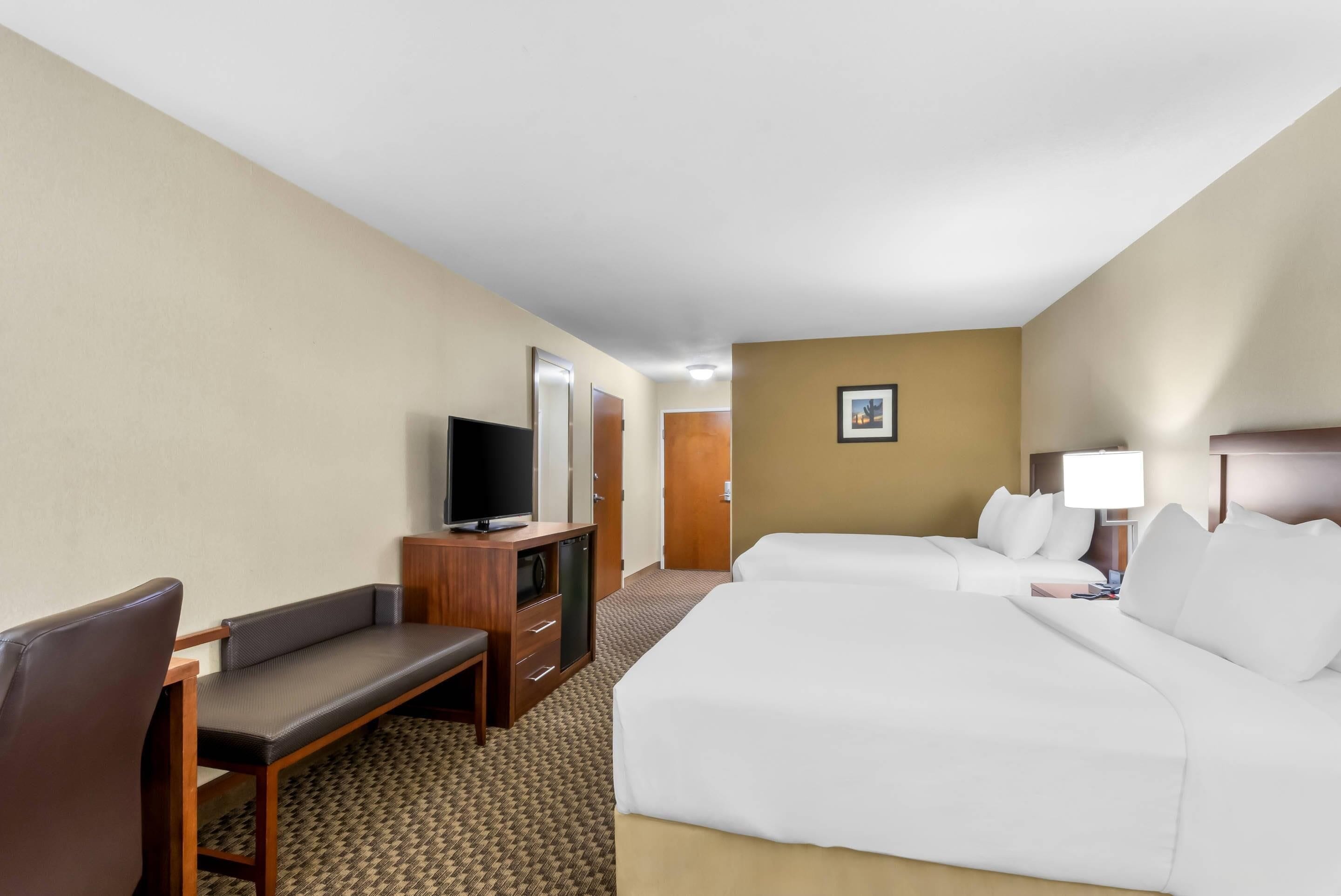 A hotel room with a bed, a desk with a television, a chair, and a door.