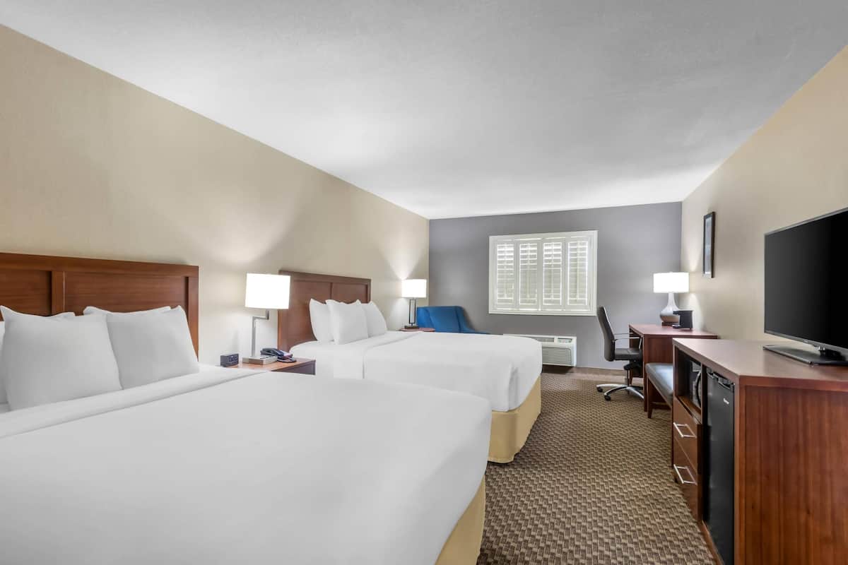A hotel room with two beds, a desk, a television, and a window with blinds.