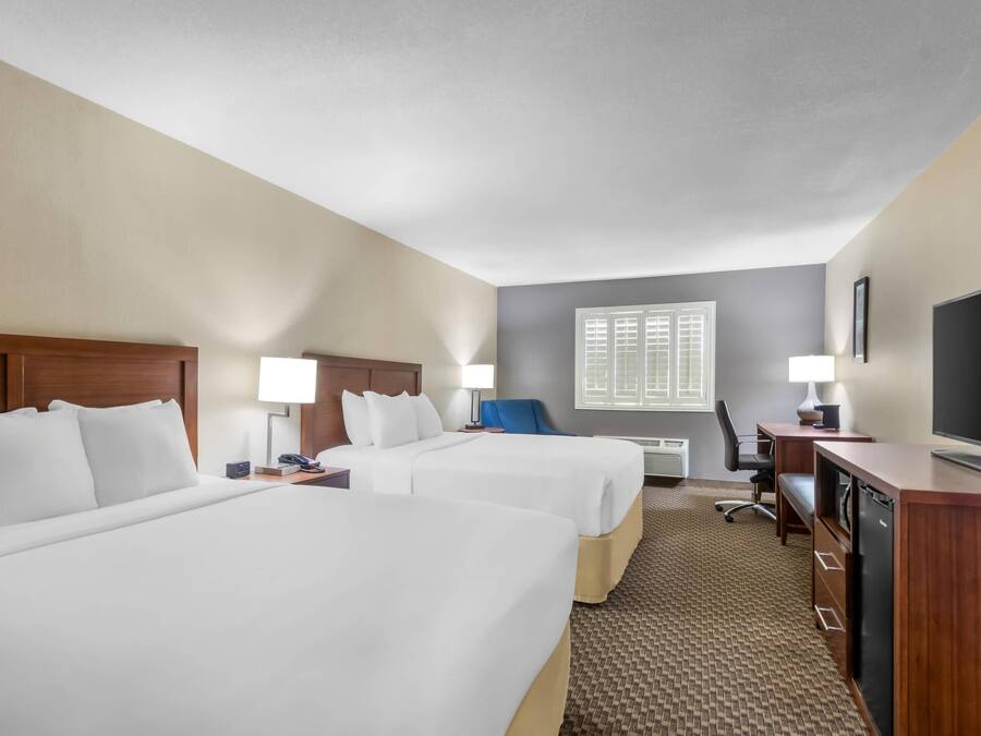 A hotel room with two beds, a desk, a television, and a window with blinds.