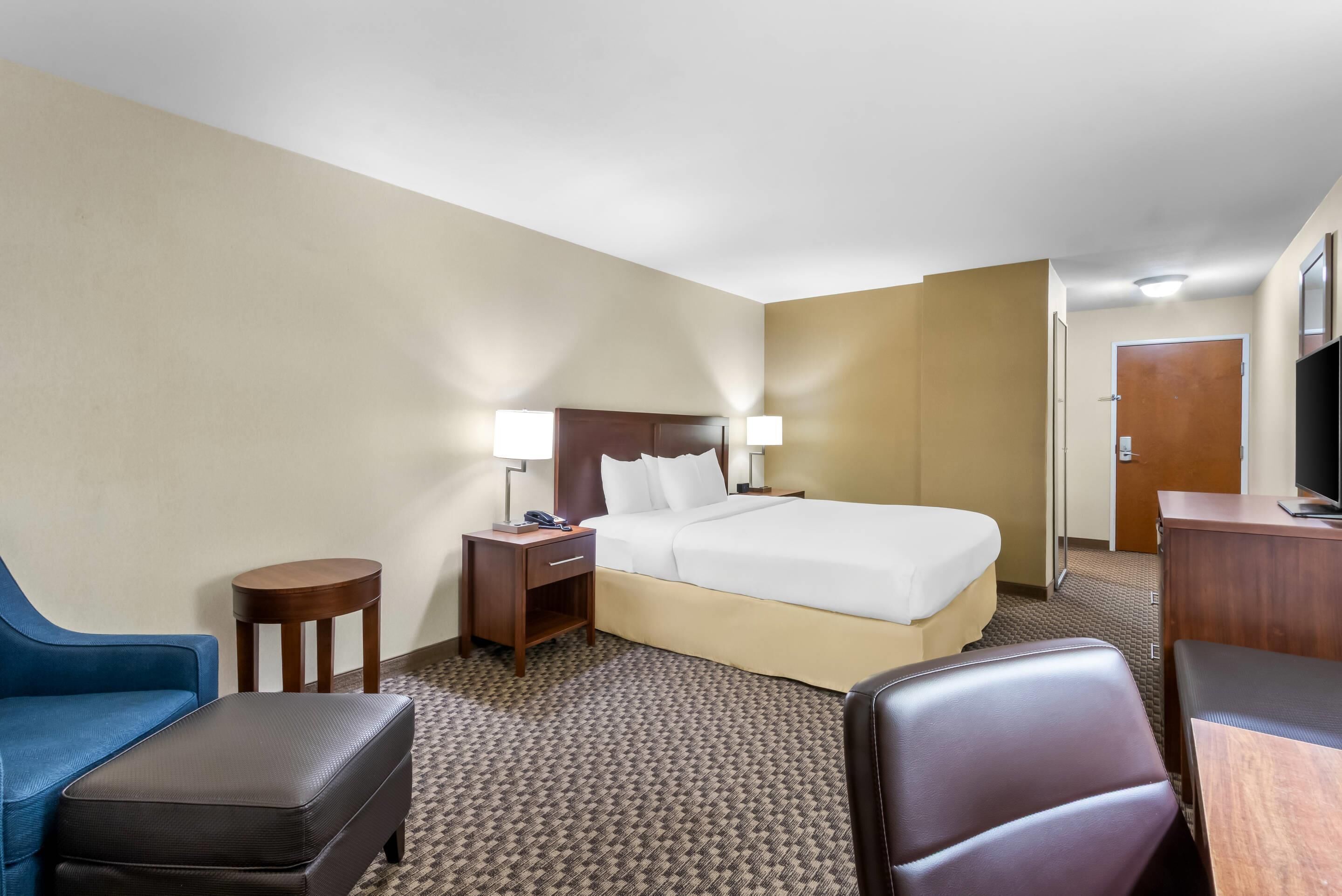 A hotel room with a bed, two bedside tables, a desk, a chair, and a blue sofa.