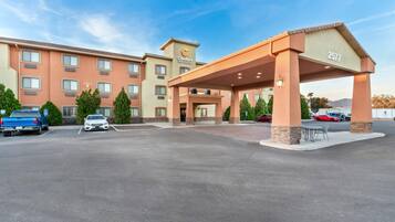 A hotel with a covered entrance, multiple parking spaces, and a clear sky.