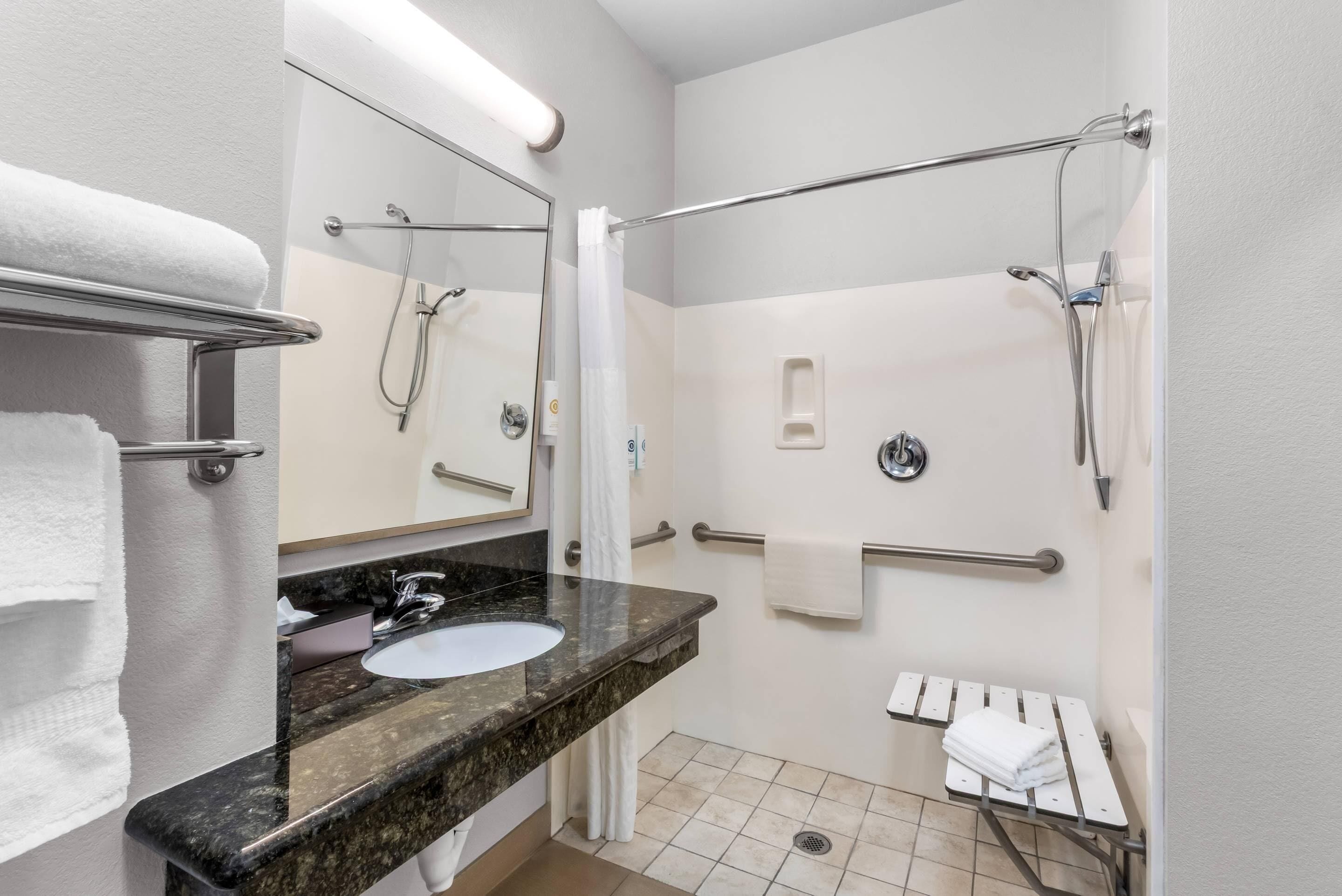 Een moderne badkamer met een wastafel met granieten blad, een spiegel, een douche met handgrepen en een handdoekhouder.