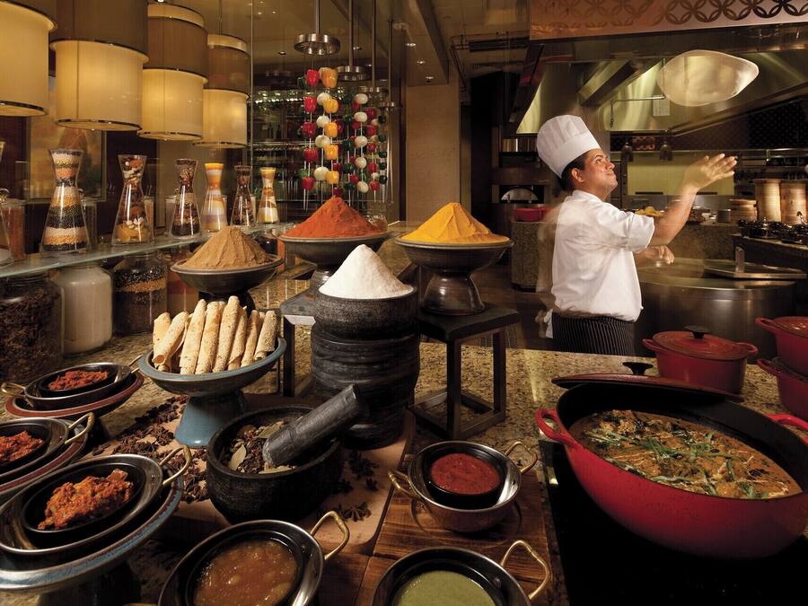 Un chef dans une cuisine professionnelle, entouré de divers ustensiles de cuisine, de casseroles et d’épices.