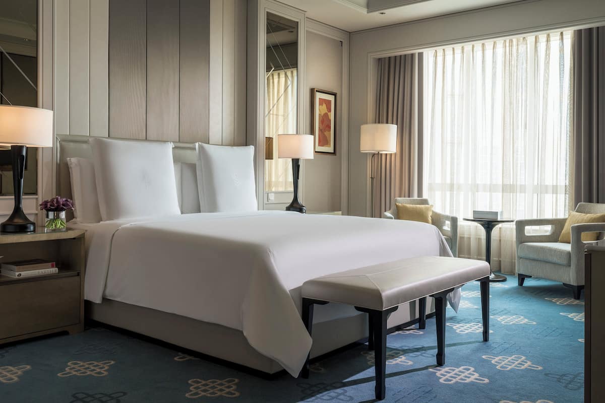 Une chambre d’hôtel avec un grand lit, deux tables de chevet, un bureau, une chaise et une fenêtre avec des rideaux.
