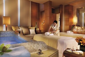 A hotel room with a spa area, including a massage table, a small pool, and a massage therapist attending to a client. - Four Seasons Hotel Macao (Cotai)