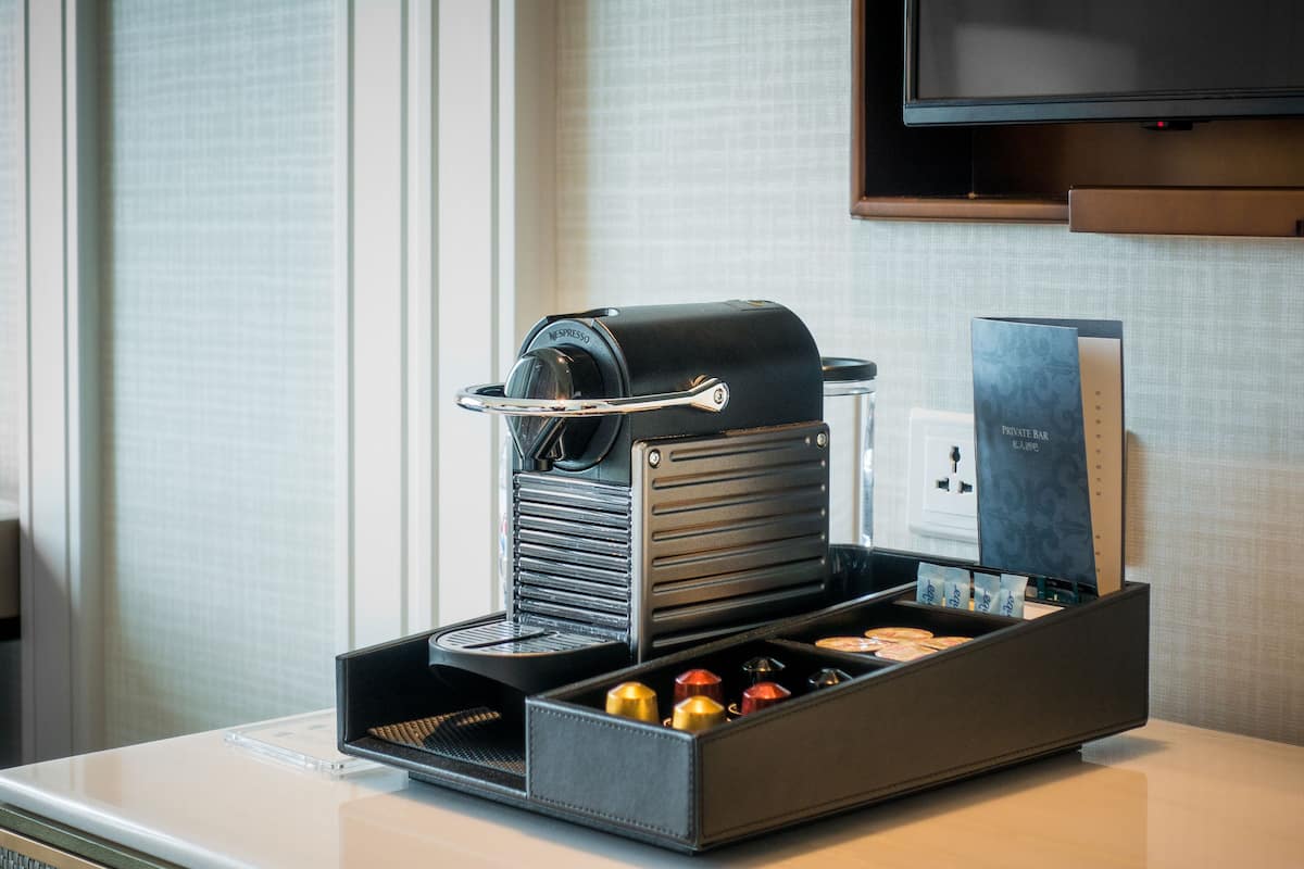 Une machine à café dotée d’un bac de récupération, d’un support pour les capsules de café et d’un présentoir pour le menu, posée sur une table d’hôtel.