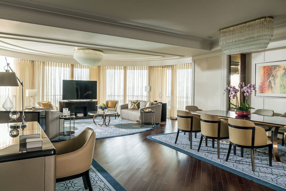 Une chambre d’hôtel moderne dotée d’une télévision à écran plat, de sièges confortables, d’un coin repas et d’une grande fenêtre avec des rideaux.