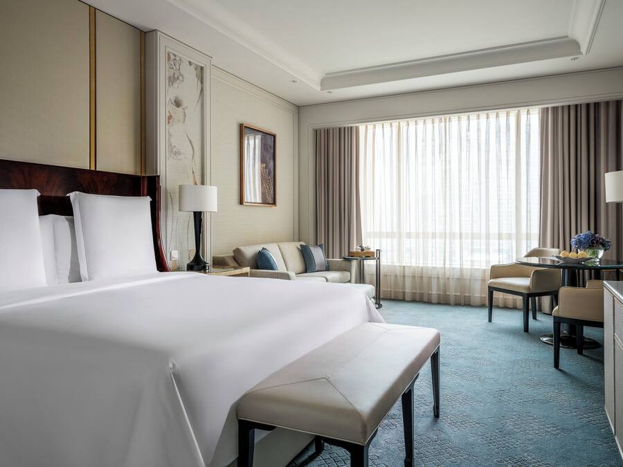 A hotel room with a large bed, a desk, a chair, and a small table with a vase of flowers.