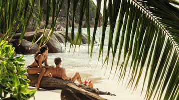 A couple sitting on a rock by the water, surrounded by greenery.