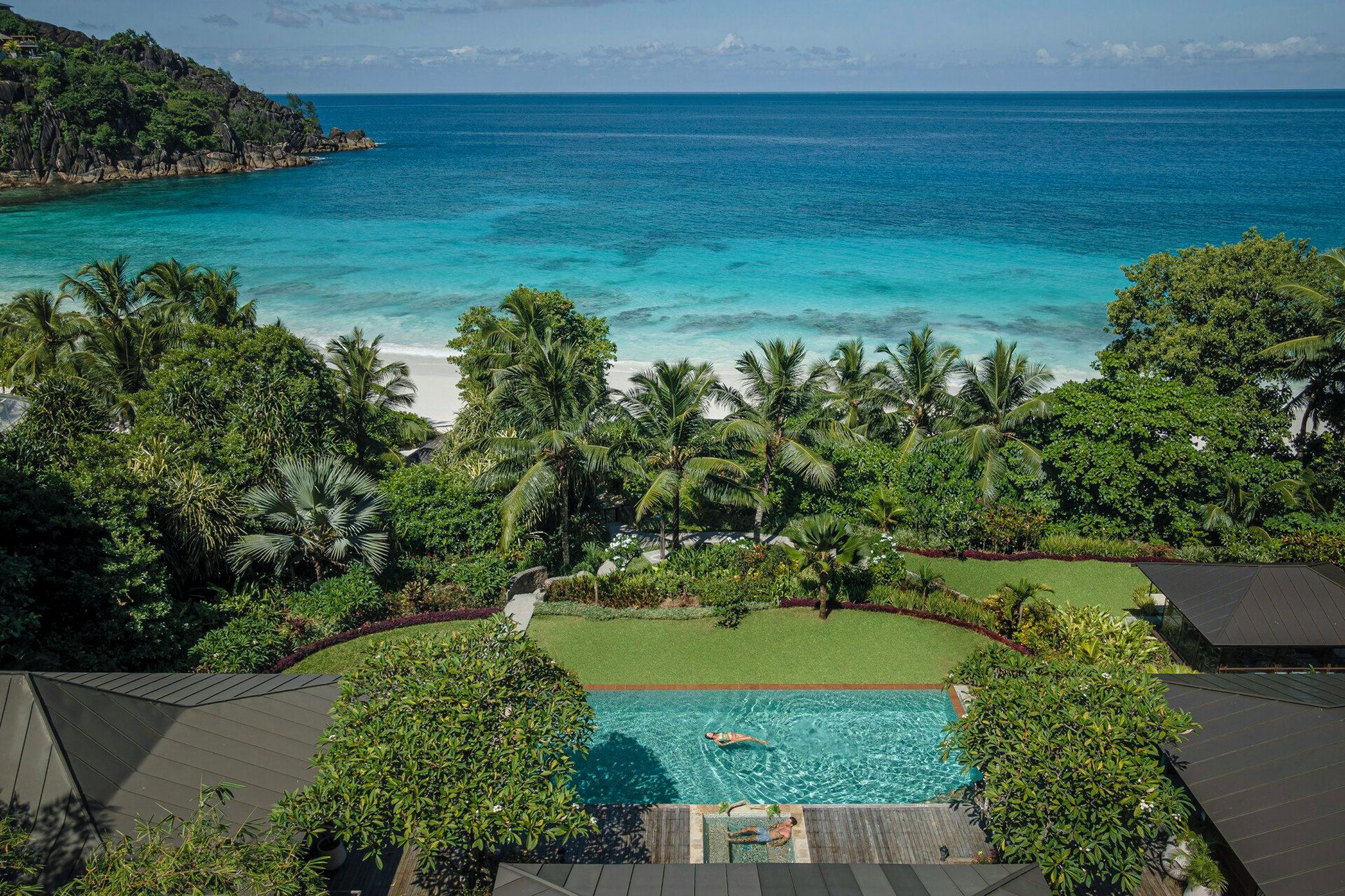 A pool with a view of the ocean, surrounded by tropical vegetation and a clear sky.