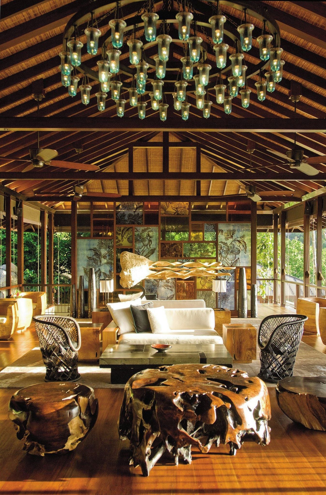 A spacious room with a high ceiling, a central seating area with a sofa and chairs, a chandelier, and a view through large windows.