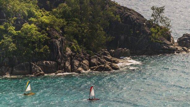 Un paysage côtier avec deux voiliers sur des eaux turquoise, entourés de falaises rocheuses et d’une végétation luxuriante.