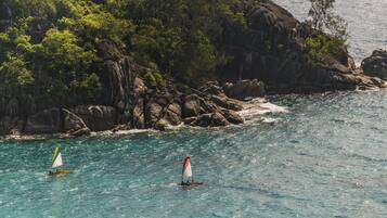 A coastal scene with two sailboats on turquoise waters, surrounded by rocky cliffs and dense greenery.