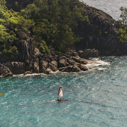 A coastal scene with two sailboats on turquoise waters, surrounded by rocky cliffs and dense greenery.