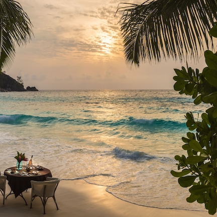 A beachside table with chairs and a table setting, overlooking the ocean.