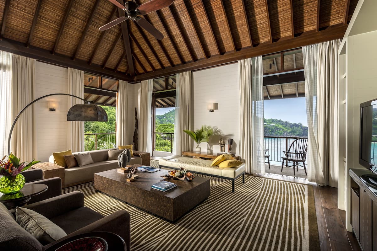 Ein großzügiges Wohnzimmer mit einer großen Couch, einem Couchtisch und einem Fernseher. Ein Balkon bietet Blick auf Wasser und Grünflächen.