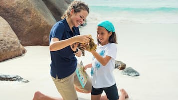 Zwei Personen an einem Sandstrand, im Hintergrund Felsen und Ozean.