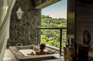 A person relaxing in a stone bathtub with a view of a lush landscape. - Four Seasons Resort Seychelles (Mahé Island)