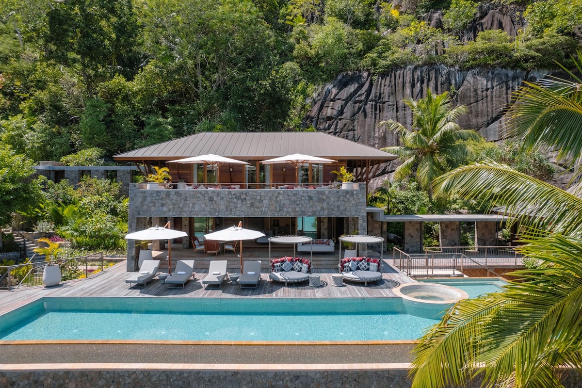 Ein modernes Resort mit Pool, Liegestühlen, Sonnenschirmen und Blick auf eine felsige Klippe.