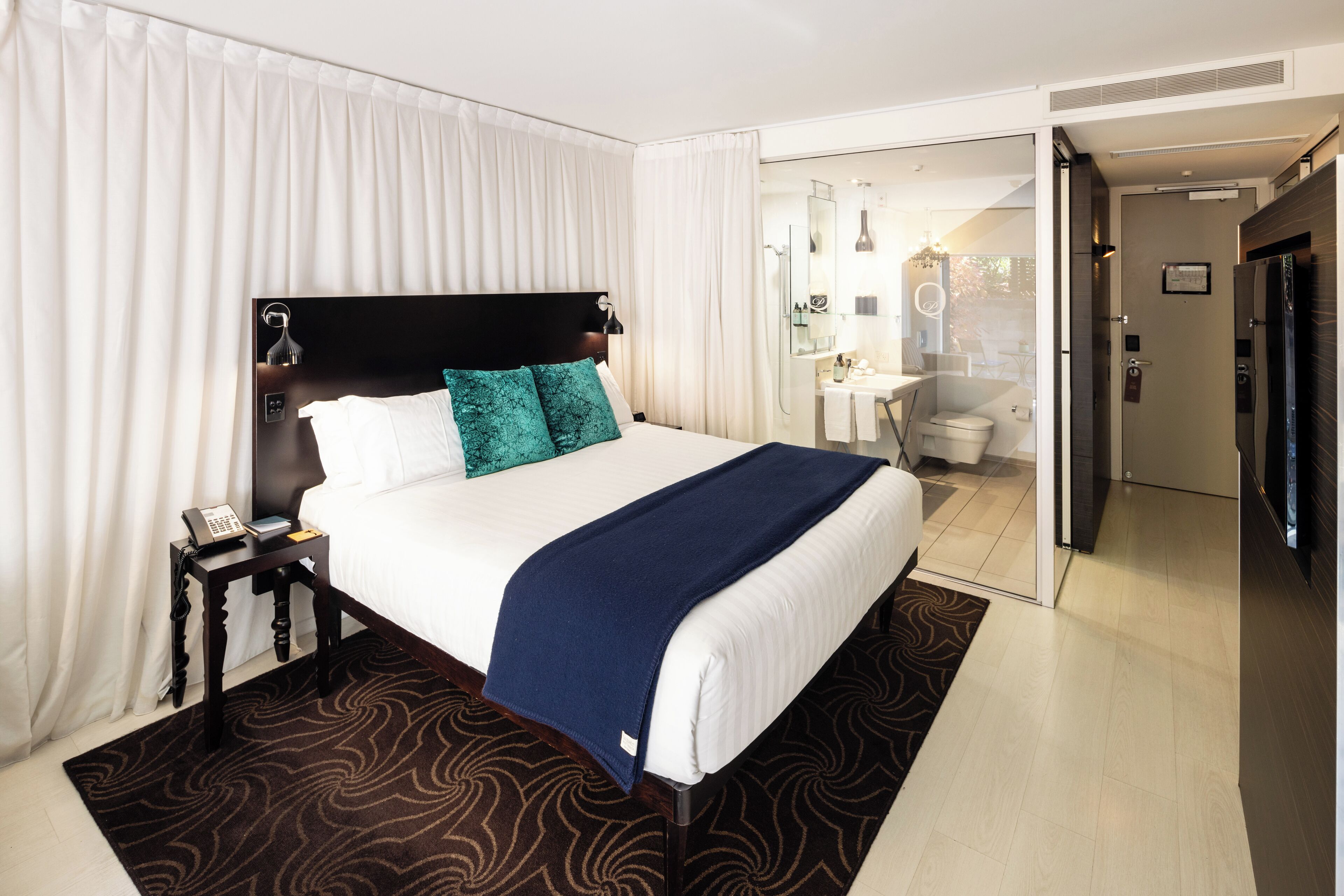 A hotel room with a large bed, a bedside telephone, and a bathroom visible through an open door.