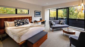 A modern bedroom with a large bed, a sofa, a desk, and a balcony with a view of greenery.
