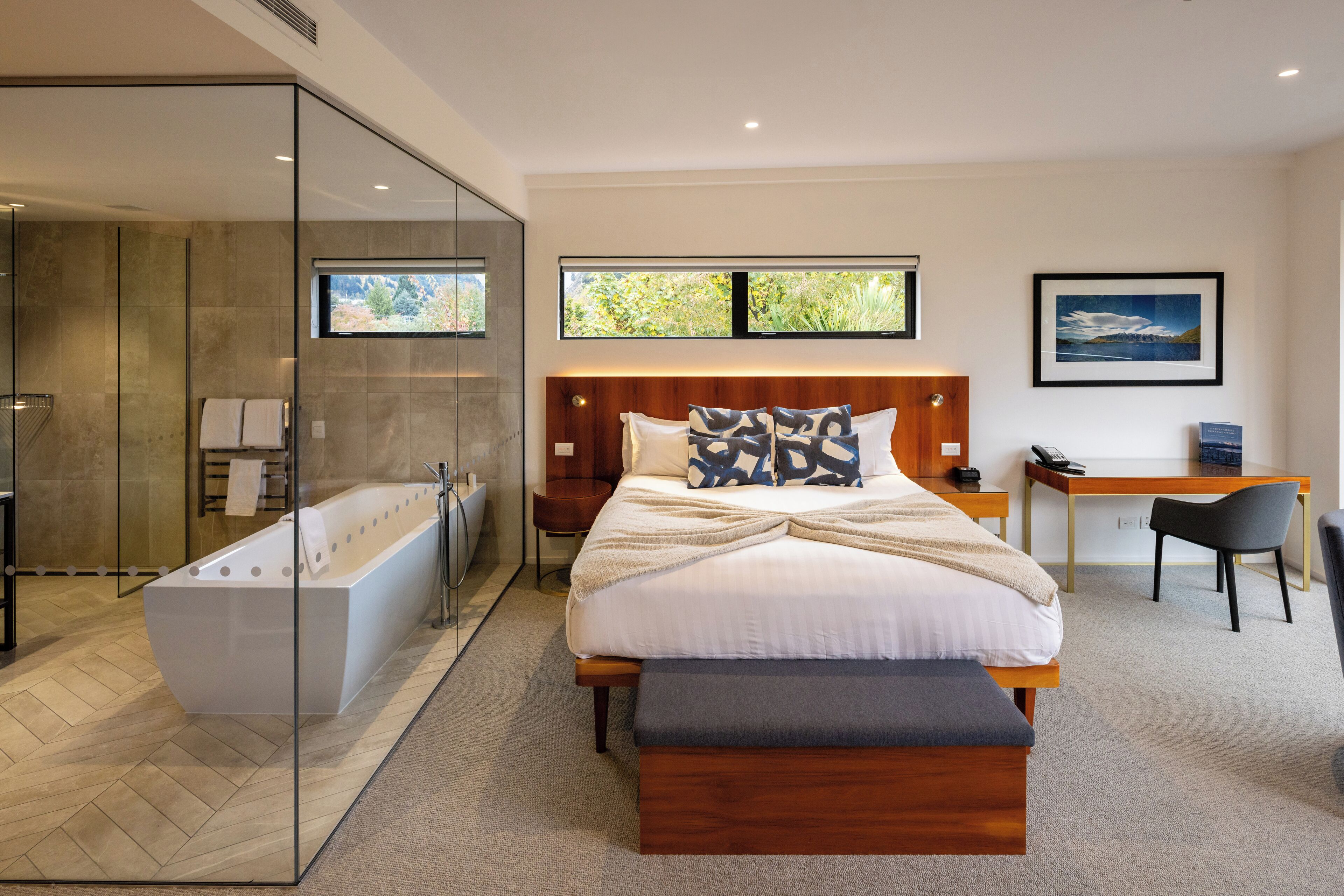 Un dormitorio moderno con una cama grande, cabecera de madera, escritorio y zona de ducha con paredes de vidrio.