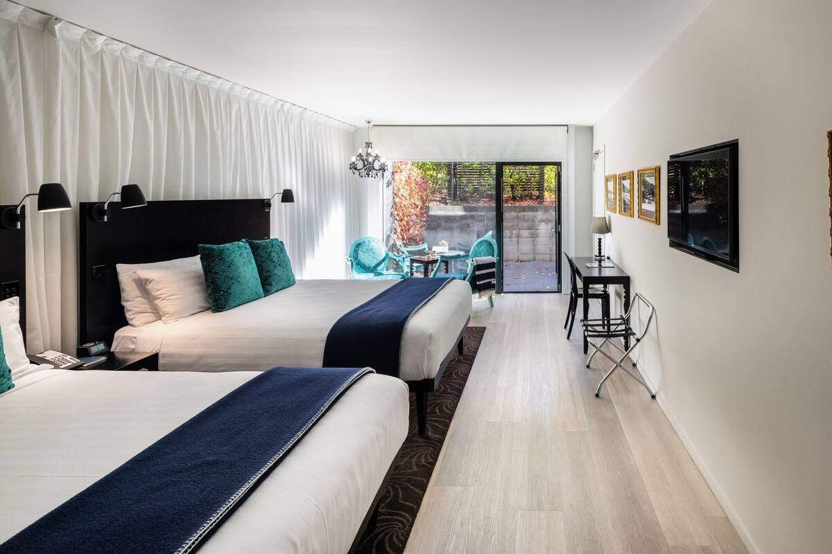 A hotel room with two beds, a balcony with a table and chairs, and a TV on the wall.