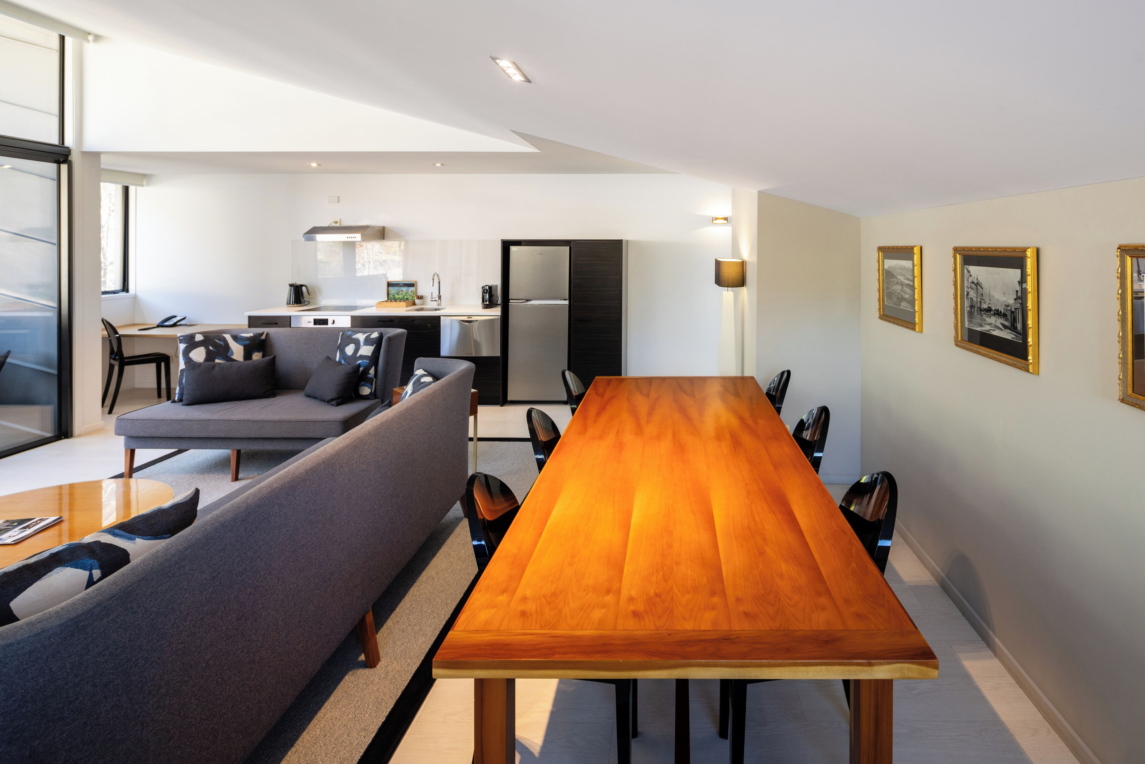 A modern living room with a dining table, sofa, and kitchen in the background.