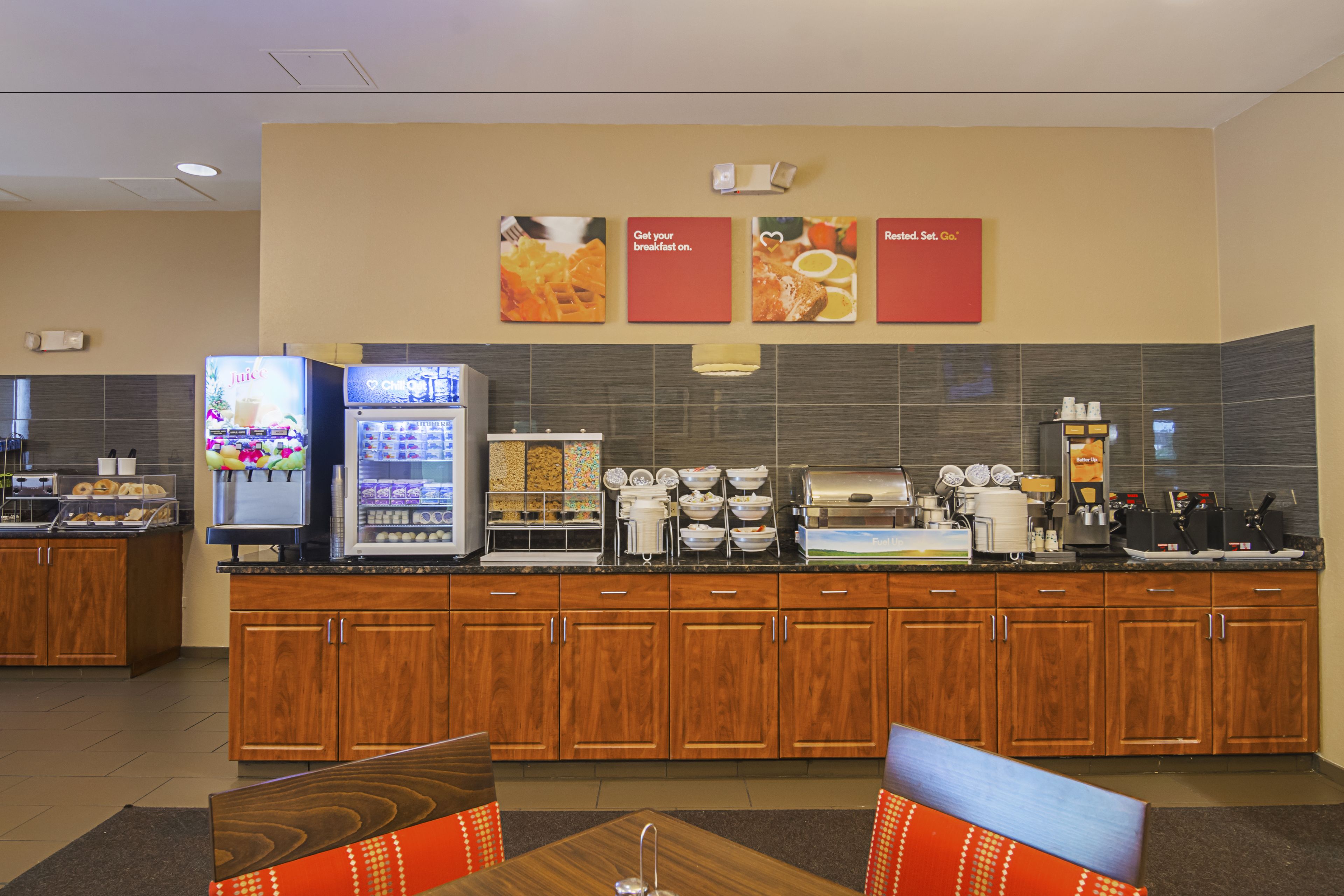 A hotel breakfast area with a self-serve station, a refrigerator, and a coffee maker.