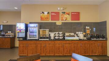 A hotel breakfast area with a self-serve station, a refrigerator, and a coffee maker.