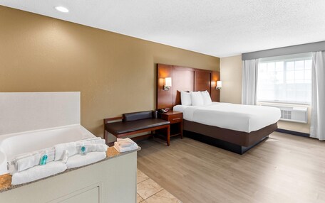 A hotel room with a bathtub, a bed, a nightstand, and a window with curtains.