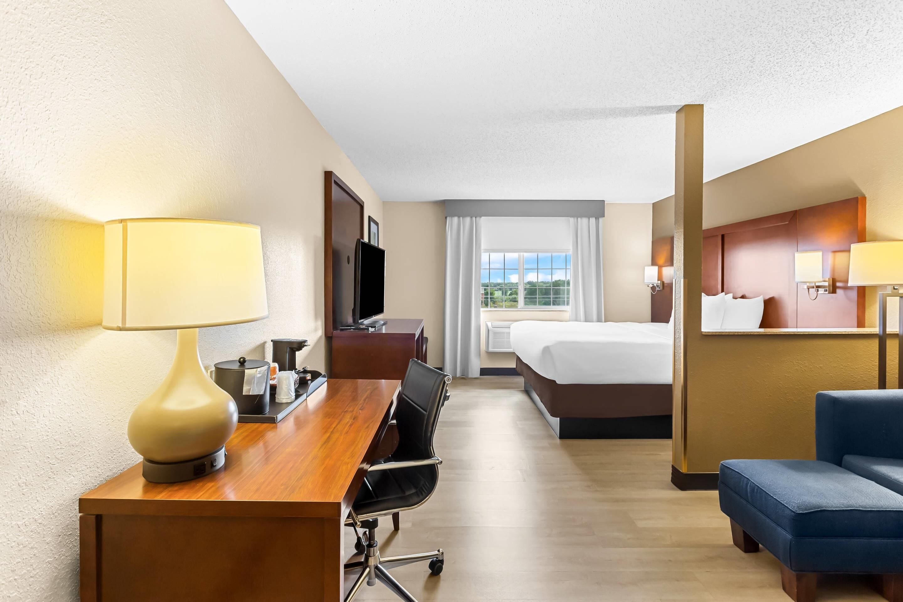 A hotel room with a desk, chair, bed, and a view of the outdoors.