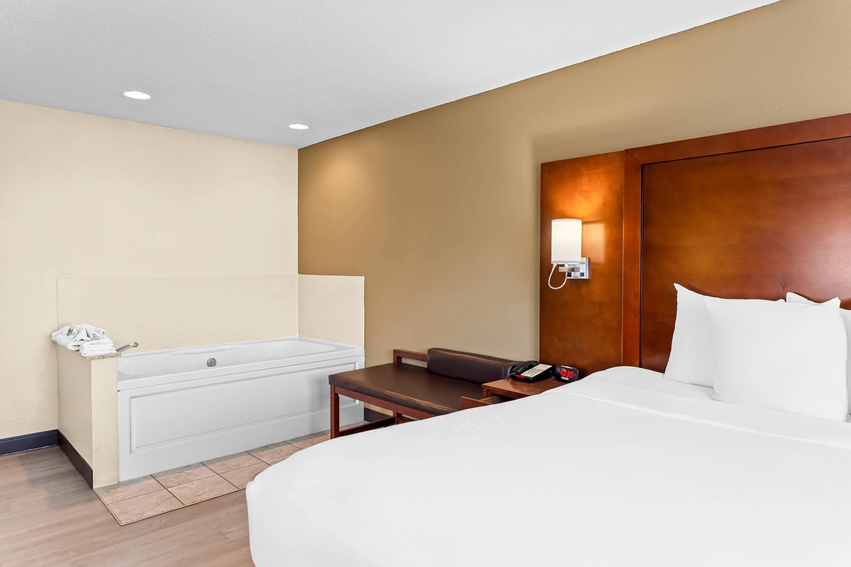 A hotel room with a bed, a desk, a chair, a bathroom, and a wall-mounted phone.