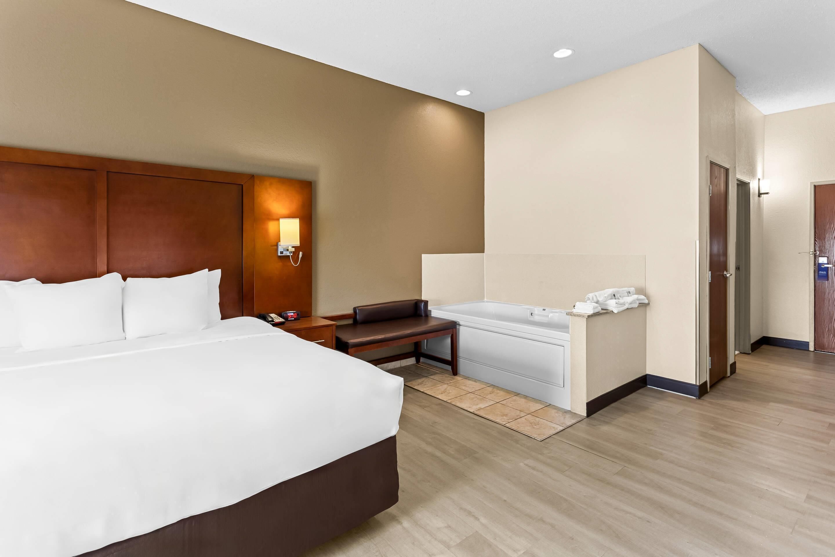 A hotel room with a large bed, a bench, a bathtub, and a desk.
