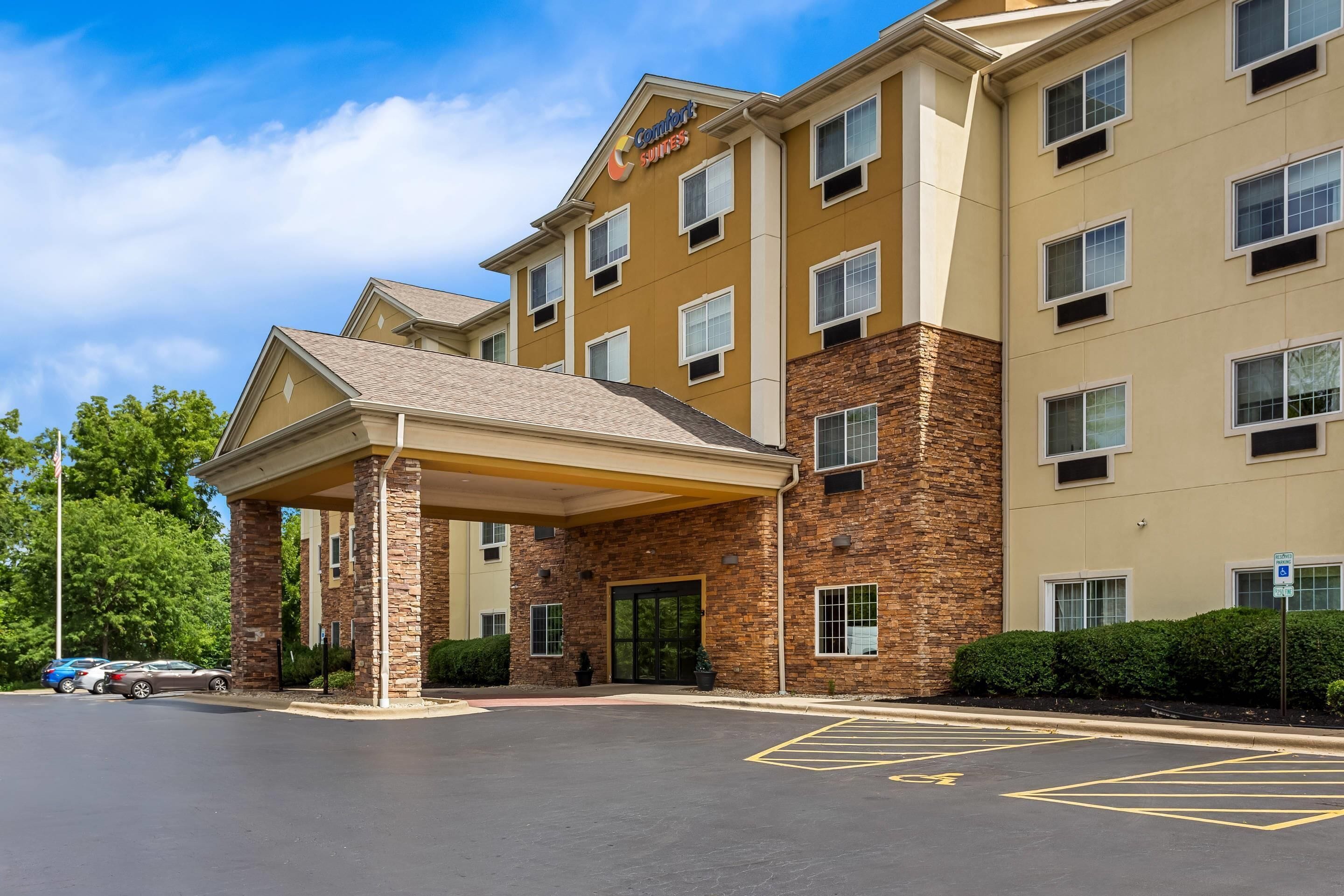 Un hôtel à la façade en briques, doté d’une entrée couverte et d’une enseigne indiquant qu’il s’agit d’un hôtel de la chaîne Comfort Suites.