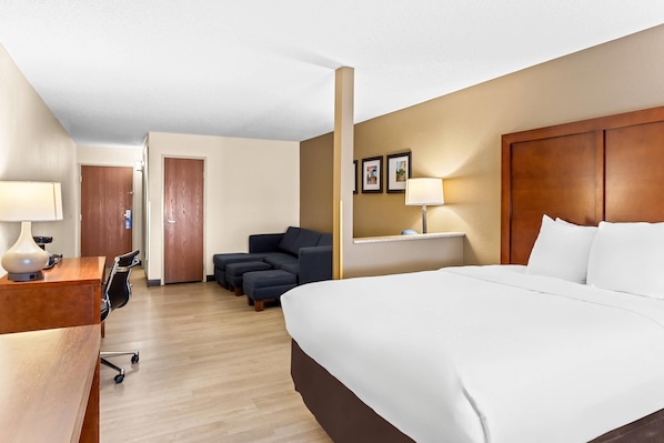 A hotel room with a bed, desk, chair, and a sofa.