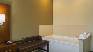 A hotel bathroom with a bathtub, a bench, a vanity with a telephone, and towels on a shelf.